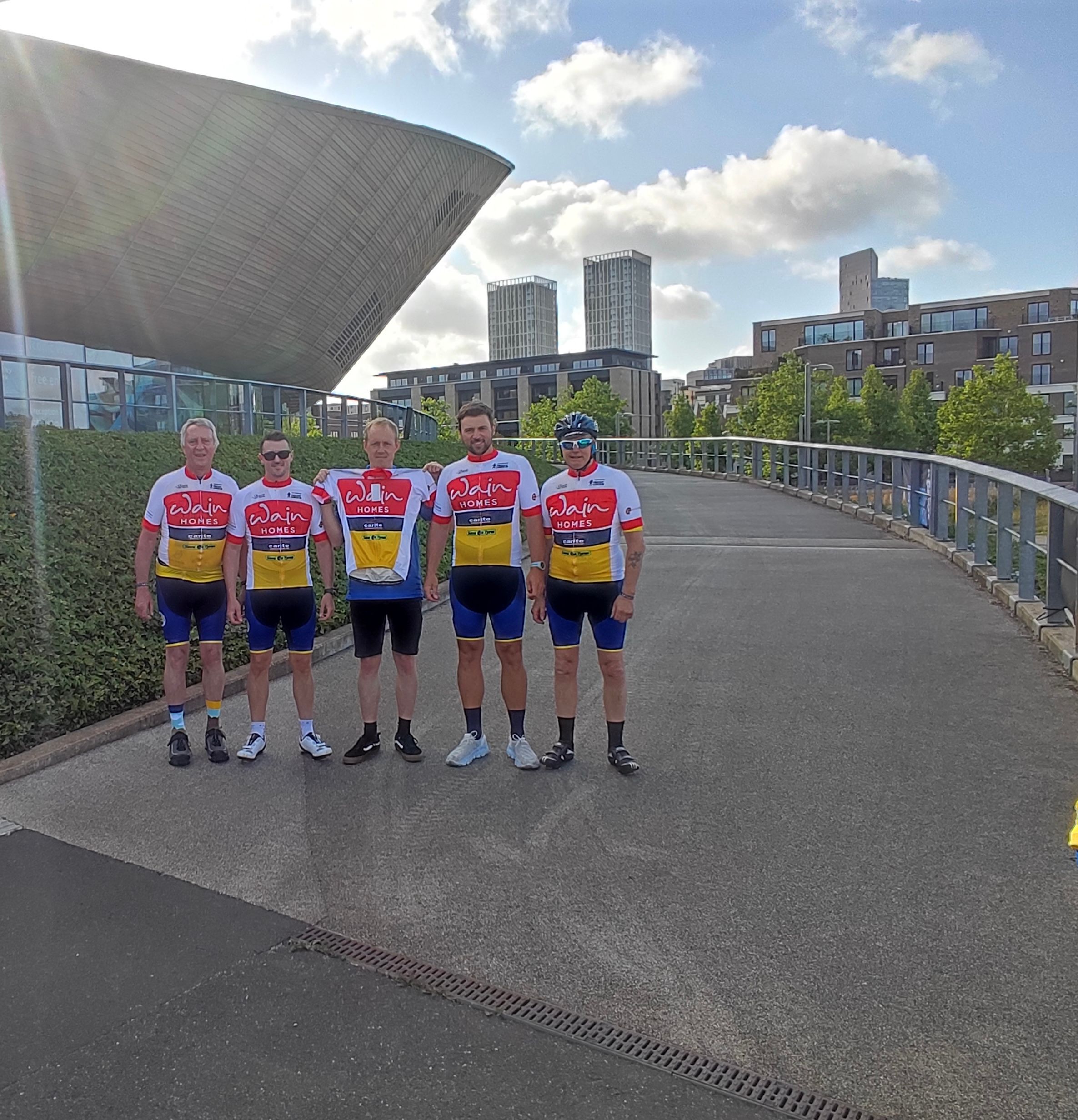 Five men are standing in cycling wear against the background of a stadium