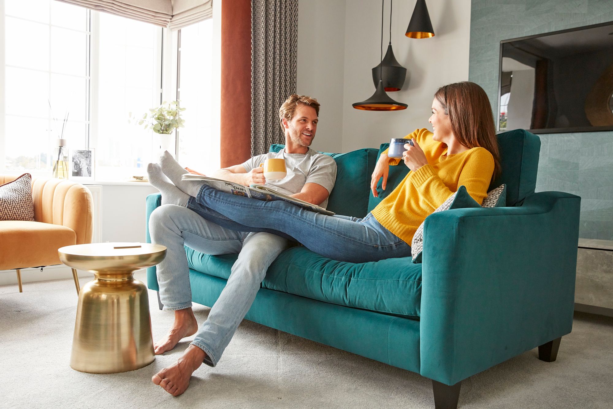 A man and a woman talking sitting on a turquoise sofa in a show home